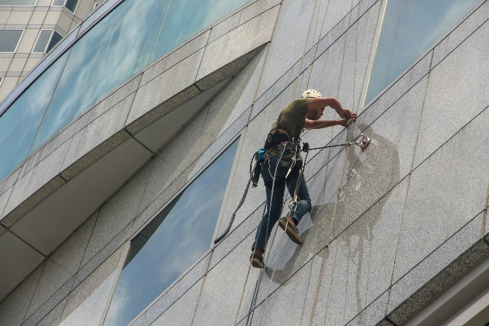Worker performing high-rise building exterior glass cleaning using rope access